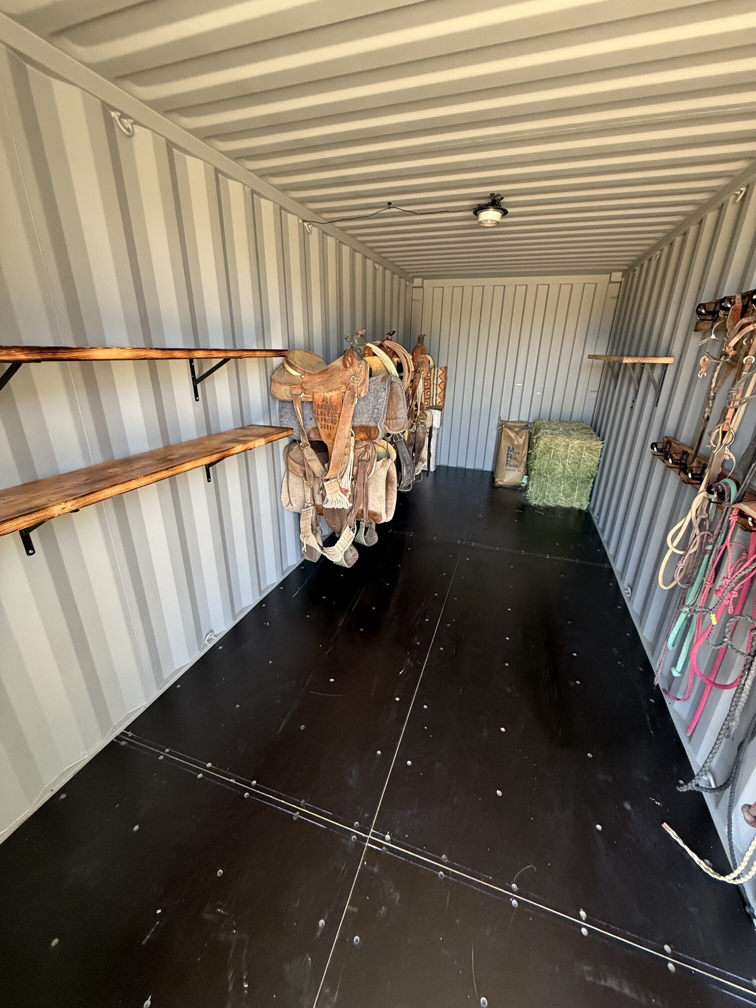 Interior of a 20-foot shipping container tack shed built by Conex Creation & Supply with saddle racks, bridle storage, shelving, and hay space for Southern Arizona ranches and horse properties.