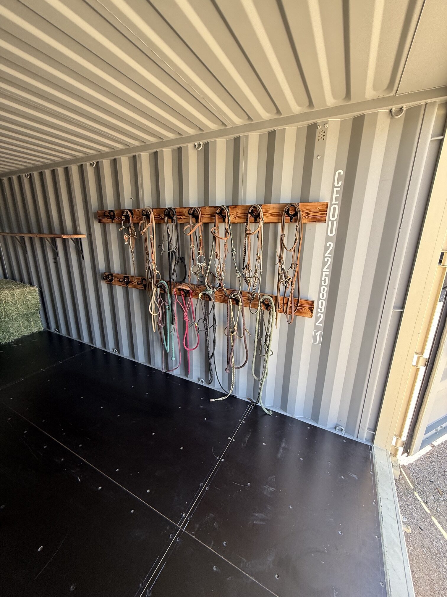 Interior of a 20-foot shipping container tack shed with 16 bridle racks mounted on wood boards for organized horse tack storage on Southern Arizona ranches.
