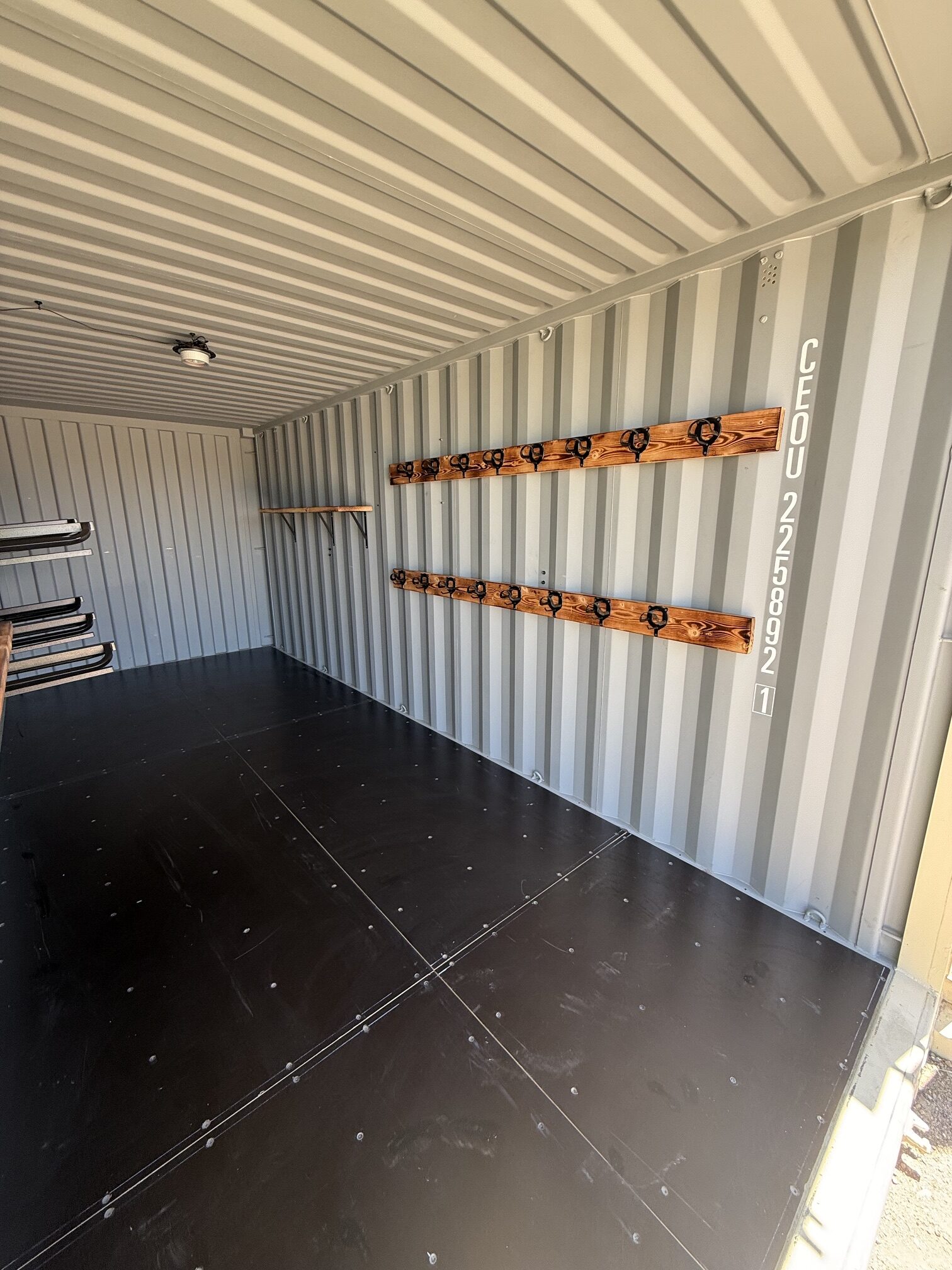 Interior of a 20-foot custom container tack shed by Conex Creation & Supply with bridle hooks, halter hangers, wood storage rails, and shelving for ranch gear in Southern Arizona.